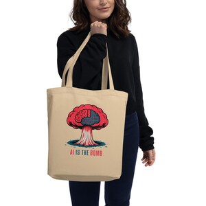 May include: Beige tote bag with a graphic of a red mushroom cloud with a brain design and the text "AI IS THE BOMB" in white. The tote bag is made of a soft material and has two handles.