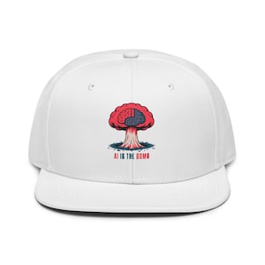 Op de afbeelding: Witte baseballpet met een platte klep. De pet heeft een afbeelding van een rode, hersenvormige explosie met de tekst "AI IS THE BOMB" in het wit. Het ontwerp is gecentreerd op de voorkant van de pet.