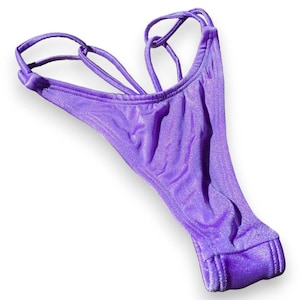 Peut inclure: Bas de bikini scintillant violet avec un design de bretelles croisées.