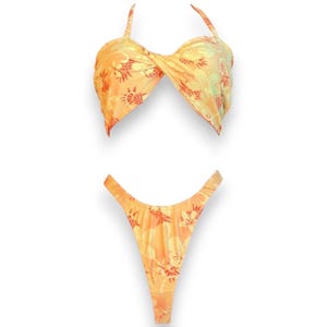 May include: A yellow and orange bikini with a tropical print. The top is a halter style with a twist detail. The bottom is a high-cut style with a cheeky back.