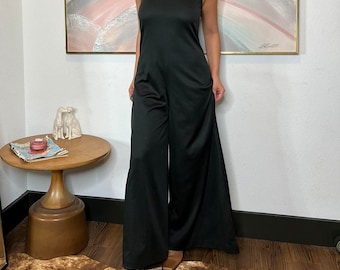 May include: A black sleeveless jumpsuit with a wide-leg silhouette. The jumpsuit has a simple, elegant design and is made from a smooth, flowing fabric.