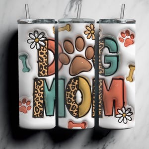 May include: Three white stainless steel tumblers with lids and straws. The tumblers are decorated with a colorful design that says "Dog Mom" with paw prints, bones, and leopard print accents.