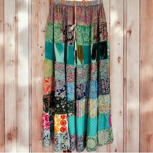 May include: A floor-length skirt featuring a patchwork design with various patterns including paisley, floral, and smiley face prints in shades of green, blue, yellow, pink, and white. The skirt has an elastic waistband with a drawstring tie.