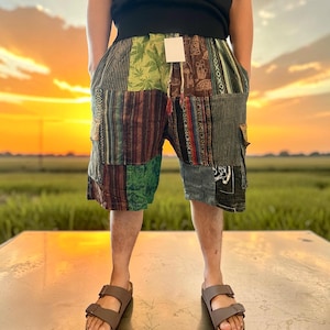 May include: Patchwork shorts featuring a variety of green, brown, and black fabric panels with diverse patterns including leaf motifs, stripes, and geometric designs. The shorts have an elastic waistband with a drawstring and side cargo pockets.