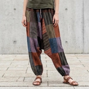 Op de afbeelding: Losvallende patchworkbroek met diverse rechthoekige stoffen panelen in bruine, blauwe, paarse en zwarte tinten. De broek heeft een taille met trekkoord, een verlaagd kruis en elastische boorden bij de enkels.