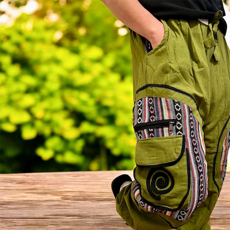 May include: Green pants with decorative pockets and a patterned design. The pockets have a zipper and a spiral design. The pants are made of a lightweight fabric and have a relaxed fit.