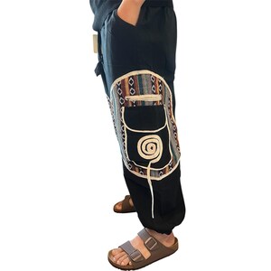 May include: Black pants with a decorative pocket featuring a colorful geometric pattern and a white spiral design. The pants have a relaxed fit and are suitable for casual wear.