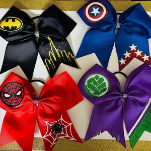 Puede incluir: Seis lazos de animadora coloridos con emblemas de superhéroes. Los lazos son negros, rojos, azules y morados. Los emblemas incluyen a Batman, Spider-Man, Capitán América y Hulk. Cada lazo tiene un centro de diamantes de imitación y una banda elástica negra.