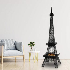 Könnte beinhalten: Schwarzer Metall-Kamin im Eiffelturm-Design. Der dekorative Kamin ist eine detaillierte Nachbildung des berühmten Wahrzeichens. Er hat ein Gittermuster und einen kleinen Feuerraum an der Basis. Der Kamin steht auf einem Holzboden.