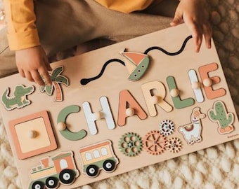 May include: A wooden personalized puzzle board with the name "CHARLIE" in colorful letters. The board features various shapes and designs, including a train, a llama, a cactus, a palm tree, a crocodile, and gears.