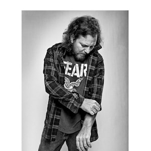 May include: A man wearing a plaid shirt over a black t-shirt with the word "FEAR" printed on it. He is wearing blue jeans.