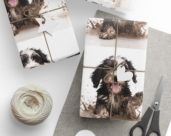 May include: Gift wrap featuring a playful black and white dog in a muddy puddle. The wrapping paper is tied with twine and adorned with a star-shaped tag. A spool of twine, scissors, and blank tags are also visible.