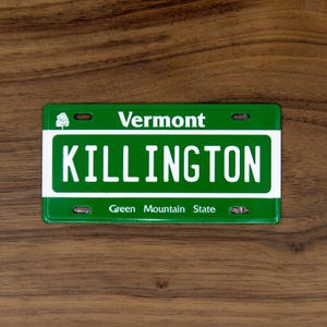 May include: A green and white Vermont license plate with the word "KILLINGTON" in bold white letters. The word "Vermont" is above the main text, and "Green Mountain State" is below. A small tree graphic is on the top left.