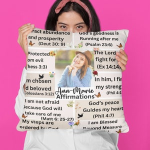 Puede incluir: Almohada blanca con un diseño colorido que incluye mariposas, flores y citas inspiradoras. La almohada tiene una foto de una mujer con una diadema floral y el texto "Ann-Marie Affirmations".