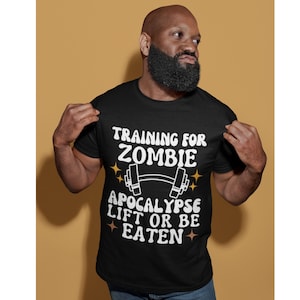 May include: Black t-shirt with white text that reads "Training for Zombie Apocalypse Lift or Be Eaten". The text is surrounded by small gold stars. A black and white dumbbell graphic is above the text.