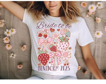 May include: White t-shirt with a pink and red strawberry design and the text "Bride to be Benidorm 2025".