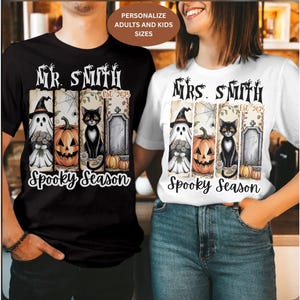 Può includere: T-shirt nere e bianche con un design a tema Halloween. Il design include un fantasma, una zucca, un gatto nero e una lapide. Il testo recita "Mr. Smith Est. 2025" e "Mrs. Smith Est. 2025" con "Spooky Season" sotto.