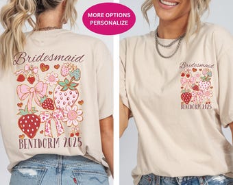 May include: A beige t-shirt with a strawberry and bow design. The shirt says "Bridemaid" and "Benidorm 2025".