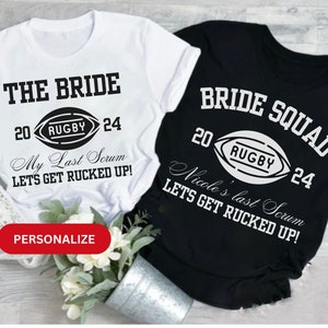 May include: Two white t-shirts with black text and a rugby ball graphic. The top shirt says "THE BRIDE 20 RUGBY 24 My Last Scrum LETS GET RUCKED UP!" The bottom shirt says "BRIDE SQUAD 20 RUGBY 24 Nicole's last Scrum LETS GET RUCKED UP!"