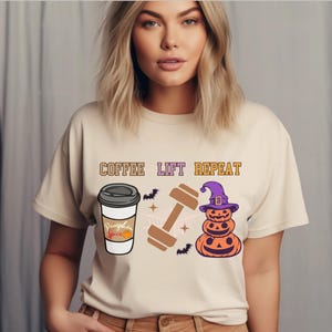 Puede incluir: Una camiseta beige con el texto "Coffee Lift Repeat" impreso en ella. El diseño también incluye una taza de café con las palabras "Pumpkin Spice" en ella, una mancuerna y una pila de tres calabazas con un sombrero de bruja.