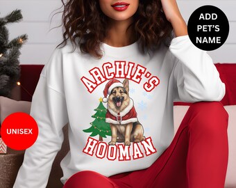 May include: White sweatshirt with a graphic of a German Shepherd dog wearing a Santa hat and standing in front of a Christmas tree. The text "Archie's Hooman" is printed on the sweatshirt.