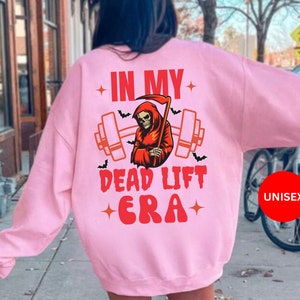 May include: Pink unisex sweatshirt with a graphic of a skeleton holding a barbell and the text "In My Dead Lift Era".