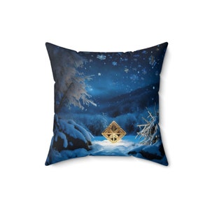 May include: A blue and white throw pillow with a snowy forest scene and a golden geometric shape in the center. The scene is illuminated by a bright light, and snowflakes are falling from the sky.