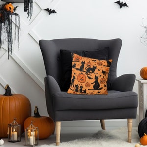 Puede incluir: Una almohada de tiro negra y naranja con un tema de Halloween. La almohada presenta gatos negros y calabazas naranjas con caras de jack-o'-lantern.
