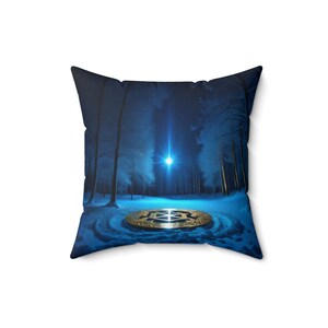 May include: A blue throw pillow with a snowy forest scene and a gold coin in the center. The coin has a symbol on it and is surrounded by a ring of snow.