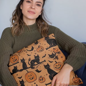 Puede incluir: Una almohada de tiro marr&oacute;n con un patr&oacute;n de tem&aacute;tica de Halloween con gatos negros, calabazas y murci&eacute;lagos. La almohada est&aacute; hecha de una tela suave y felpa y tiene un brillo sutil.