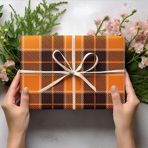 May include: A gift box wrapped in orange and brown plaid paper with a white ribbon tied in a bow.