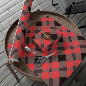 May include: A red and black buffalo plaid wrapping paper with a matching gift box and a roll of wrapping paper. The gift box is tied with a brown ribbon and a brown bow. A pair of scissors and a roll of tape are also included.
