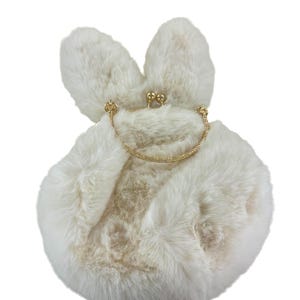 May include: A fluffy, cream-colored handbag shaped like a bunny. The bag features long, upright ears and a rounded body. A gold-colored chain handle and clasp add a touch of elegance. The bag is made of soft, faux fur material.