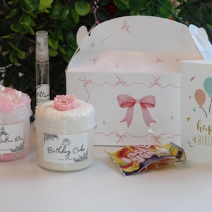 Könnte beinhalten: Ein Geburtstagsgeschenk-Set mit zwei Slime-Gläsern mit den Aufschriften "Rainbow Balloon Bliss" und "Birthday Cake", einer Parfümflasche, einer Geschenkbox mit rosa Schleife, einer Geburtstagskarte mit Ballons und einer Süßigkeitenpackung.