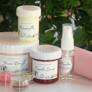 Könnte beinhalten: Eine Sammlung von Slime-Zubehör, darunter Behälter mit den Aufschriften "Pizza Dough", "Tomato Sauce" und "Mozzarella". Außerdem eine Sprühflasche mit der Aufschrift "Aktivator", kleine Behälter mit farbigem Slime und eine rosa Teigrolle.