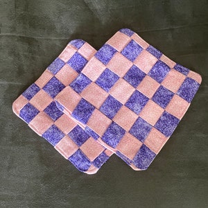 May include: Two pink and purple checkered fabric pot holders. The fabric is a woven pattern with a floral design.