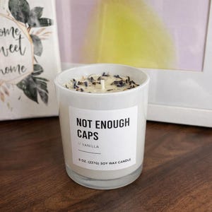 May include: A white soy wax candle in a clear glass jar. The candle has a label that reads "NOT ENOUGH CAPS // VANILLA". The candle is topped with dried lavender and has a single wick. The candle is 8 oz (227g).