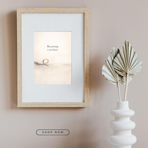 May include: A framed print with the text "Becoming is not linear." The artwork features a minimalist design with a light background and a simple line drawing. A white vase with dried palm leaves is to the right.