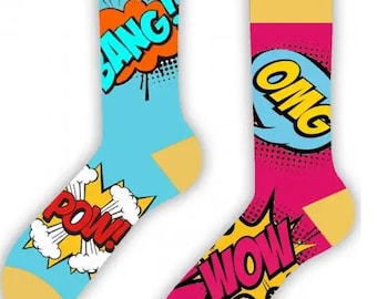 Puede incluir: Un par de calcetines coloridos con temática de cómics. Un calcetín es azul con texto amarillo, naranja y rojo que dice "BANG!" y "POW!" El otro calcetín es rosa con texto amarillo, azul y rojo que dice "OMG!" y "WOW!"