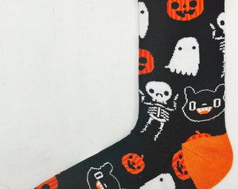 Puede incluir: Calcetines negros con puño naranja y un patrón de temática de Halloween con calabazas, fantasmas, esqueletos y gatos.