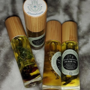 Op de afbeelding: Vier kleine glazen flesjes met houten dopjes gevuld met een gele vloeistof en verschillende kruiden en bloemen. De flesjes zijn gelabeld met "Herb-Infused Oil Roll-On" en "Olive Oil, Jojoba Oil, Castor Oil, Herbs".
