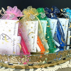 May include: A collection of colorful mesh bags filled with various items, including scrolls and candles. Each bag is adorned with a charm and a tag with text such as "Love" and "Ignites Passion". The bags are arranged in a decorative, gold-toned tray.