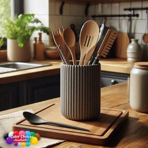 May include: A cylindrical grey utensil holder with a vertical ribbed texture, containing various wooden kitchen tools including a spoon, a slotted turner, and a spatula. A black spoon rests on a wooden cutting board next to the holder.