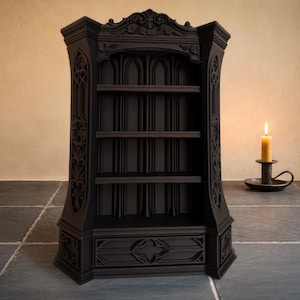 May include: A black, gothic-style bookcase with three shelves and decorative carvings. The bookcase features arched window-like openings. A lit candle in a black candlestick holder is positioned to the right of the bookcase.