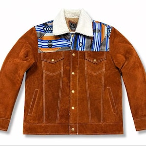 May include: A brown suede jacket featuring a white sherpa collar and a patterned yoke across the chest. The yoke displays blue, orange, and black geometric designs. The jacket includes gold-toned metal buttons, two chest pockets, and side pockets.