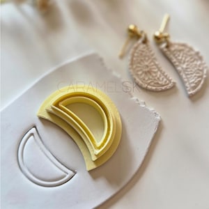 May include: A craft image featuring a yellow crescent-shaped clay cutter and a matching earring set. The earrings and cutter are on a white surface. The text "CARAMELSKY" is visible.