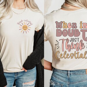 Puede incluir: Una camiseta de color crema con el texto "When in doubt, just think celestial!" en la parte posterior y un sol con una cara sonriente y el texto "Think celestial" en la parte delantera.