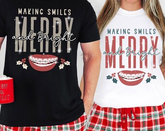 May include: Black and white t-shirts with the text "MAKING SMILES MERRY and BRIGHT" and a graphic of a smiling mouth with braces. The shirts are paired with red and green plaid pajama pants. One person holds a red mug.