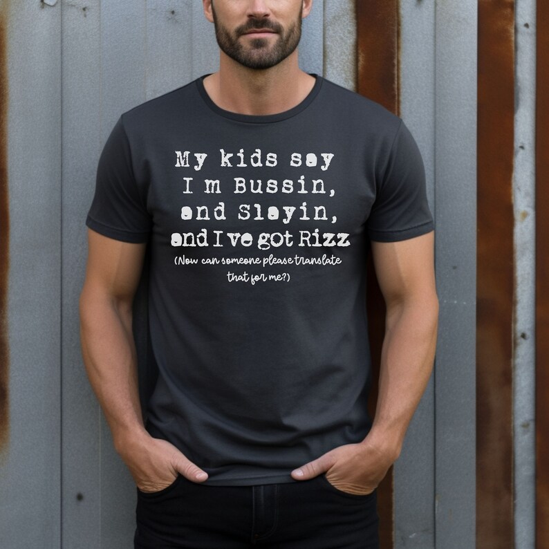 May include: Dark gray t-shirt with white text that reads "My kids say I'm Bussin, and Slayin, and I've got Rizz (Now can someone please translate that for me?)". The shirt is a crew neck style.