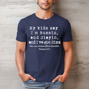 May include: Navy blue t-shirt with white text that reads "My kids say I'm Bussin, and Slayin, and I've got Rizz (Now can someone please translate that for me?)". The shirt is made of a soft material.